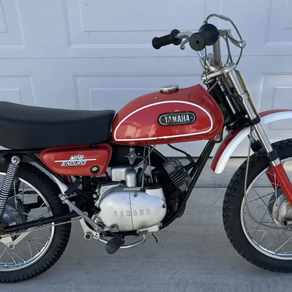 Seitenansicht einer Yamaha JT1 Mini Enduro von 1971 in Desert Orange, mit schwarzem Sitz und klassischen Offroad-Elementen.