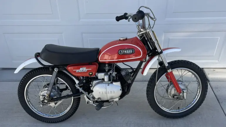 Seitenansicht einer Yamaha JT1 Mini Enduro von 1971 in Desert Orange, mit schwarzem Sitz und klassischen Offroad-Elementen.