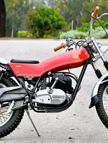 Seitenansicht einer roten 1972 Montesa Cota Enduro Trials mit Geländeprofil, abgestellt auf Asphalt.