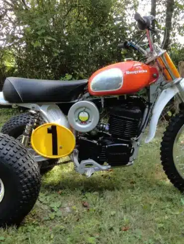 1973 Husqvarna Super Cycle 450 CR 3-Wheeler mit rotem Tank und gelber Startnummer im Gras stehend