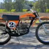 1974 Carabella 125 Motocross im Originalzustand, Seitenansicht mit orange-schwarzem Tank und Startnummer 27.