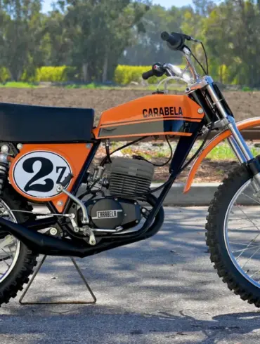 1974 Carabella 125 Motocross im Originalzustand, Seitenansicht mit orange-schwarzem Tank und Startnummer 27.