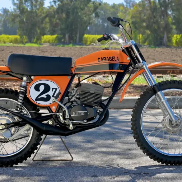 1974 Carabella 125 Motocross im Originalzustand, Seitenansicht mit orange-schwarzem Tank und Startnummer 27.