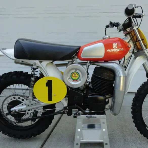 Seitenansicht einer 1974 Husqvarna 400 CR Motocross-Maschine mit rotem Tank und Startnummernschild.