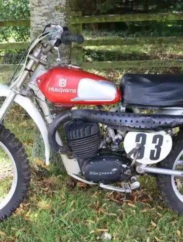 Seitenansicht einer Husqvarna 250 Cross von 1967 mit rotem Tank und Startnummer 33 auf grasbewachsenem Untergrund