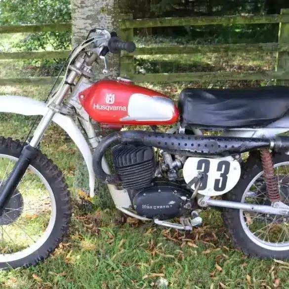 Seitenansicht einer Husqvarna 250 Cross von 1967 mit rotem Tank und Startnummer 33 auf grasbewachsenem Untergrund