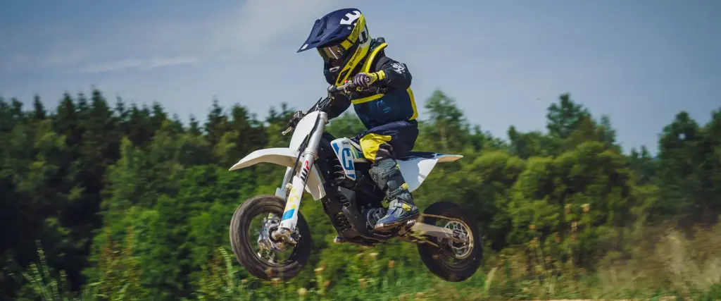 Kind fährt Husqvarna EE 3 E-Motocross über eine Offroad-Strecke im Grünen.