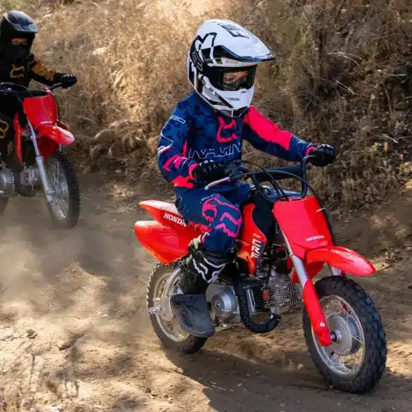 Kinder fahren mit der Honda CRF50F auf einer staubigen Offroad-Strecke.