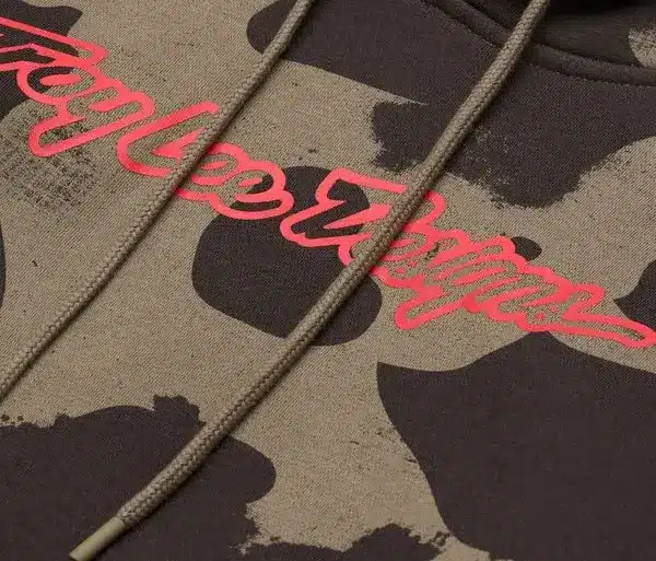 Detailfoto eines olivgrünen Camouflage-Kapuzenpullovers mit auffälligem Troy Lee Designs Schriftzug