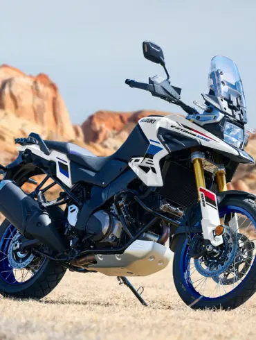 Suzuki V-Strom 1050DE Motorrad, stehend im Gelände vor Felsen, Seitenansicht