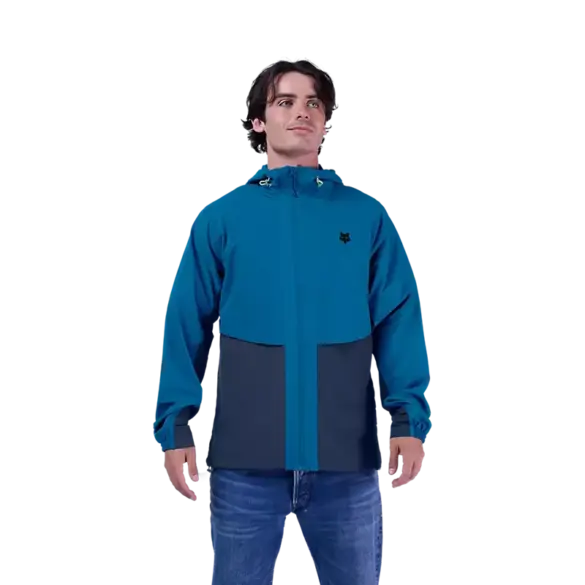 Ein Mann trägt die blaue Survivalist Windjacke mit Kapuze und Reißverschluss.