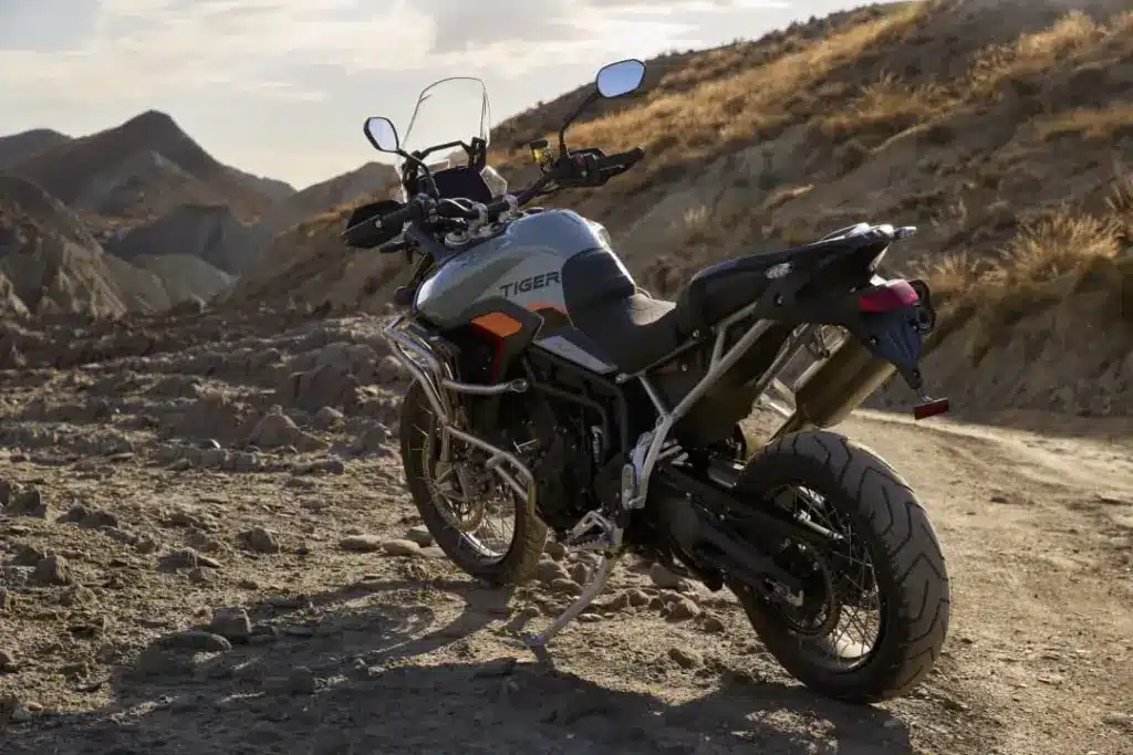 Triumph Tiger 900 Desert Edition steht auf einer staubigen Offroad-Piste in bergiger Landschaft.
