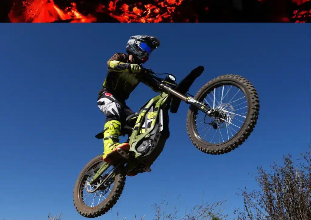 Fahrer springt mit einer Sur-Ron Light Bee X Elektro-Enduro über eine Geländestufe bei blauem Himmel.