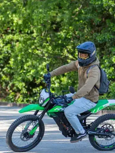 Person fährt eine grüne Rieju e-Tango Elektro-Enduro auf einer Straße, umgeben von Bäumen