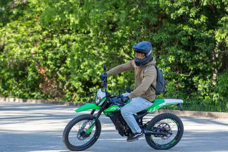 Person fährt eine grüne Rieju e-Tango Elektro-Enduro auf einer Straße, umgeben von Bäumen