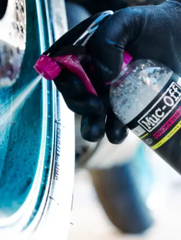 Sprühflasche mit Motorradfelgenreiniger wird auf eine verschmutzte Felge aufgetragen