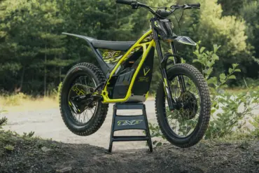 Triumph TXP-24 Elektromotorrad im Offroad-Einsatz auf einem Ständer vor Waldkulisse