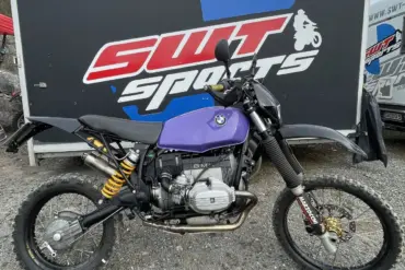 Seitenansicht des SWT-SPORTS EnduroBoxer Nr. 150, einem modifizierten BMW R 80 G/S Motorrad mit lila Tank und Geländebereifung vor einem SWT-SPORTS Anhänger.