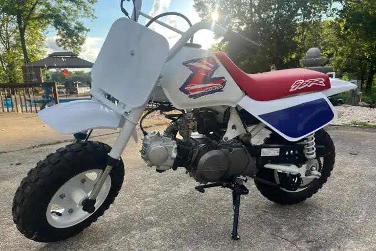 Restaurierte Honda Z50 von 1995 mit weiß-blau-rotem Farbschema, originalem Tank, rotem Sitz und korrekt angebrachtem Z-Logo, abgestellt im Außenbereich.