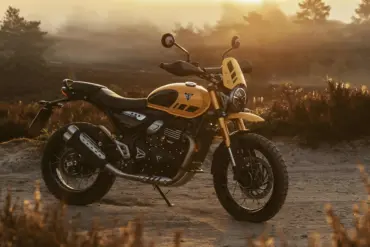 Triumph Scrambler 400 XC in Gelb steht offroad im Abendlicht vor Büschen und Bäumen.