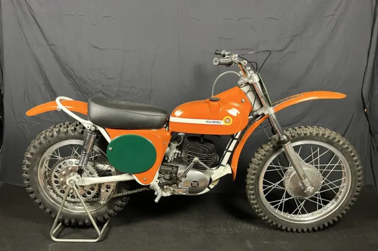 Seitenansicht einer restaurierten orangefarbenen Montesa 250 GP (Cappra) von 1968 vor dunklem Hintergrund.