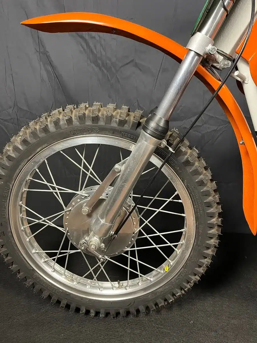 Nahaufnahme vom Vorderrad und Vorderradgabel einer restaurierten Montesa 250 GP aus dem Jahr 1968 mit orangefarbenem Schutzblech.