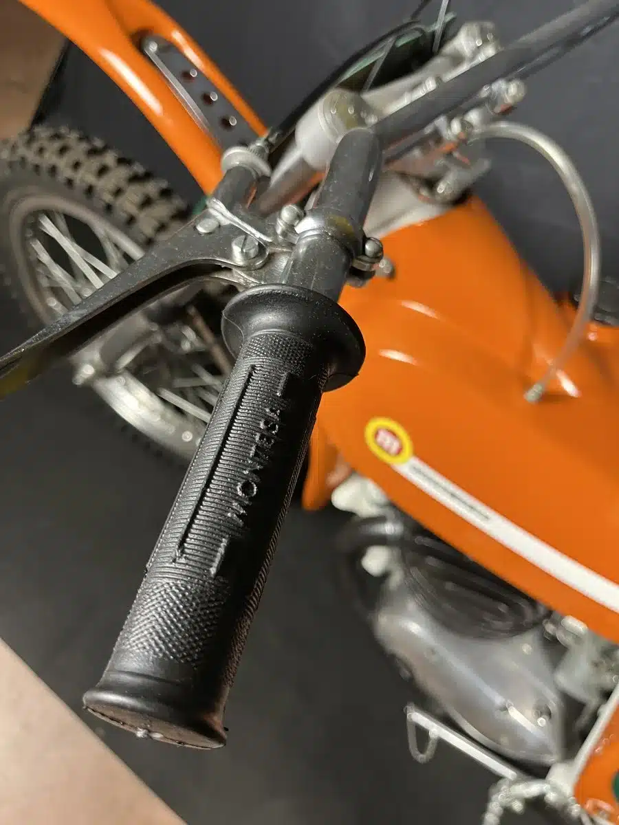Nahaufnahme des Lenkers und Gasgriffs einer orangefarbenen Montesa 250 GP von 1968, restauriertes Motocross-Motorrad.