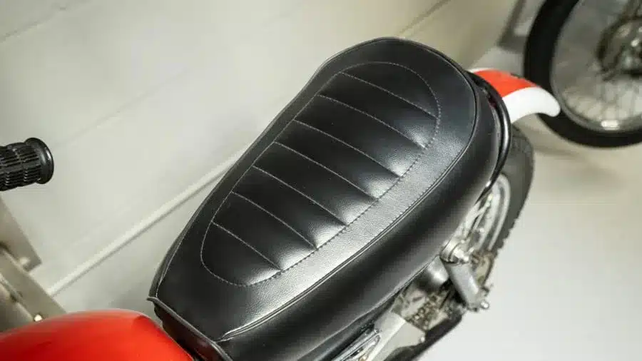 Schwarze, gesteppte Sitzbank einer Yamaha Mini Enduro MX von 1970 mit rotem Heckkotflügel im Hintergrund.