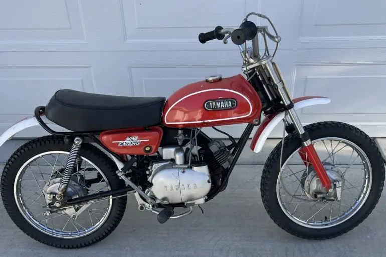 Seitenansicht einer Yamaha JT1 Mini Enduro von 1971 in Desert Orange, mit schwarzem Sitz und klassischen Offroad-Elementen.