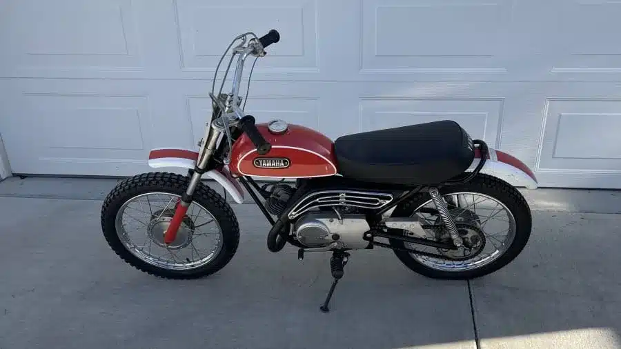 Seitenansicht einer Yamaha JT1 Mini Enduro aus dem Jahr 1971 mit orangefarbenem Tank und Offroad-Bereifung.
