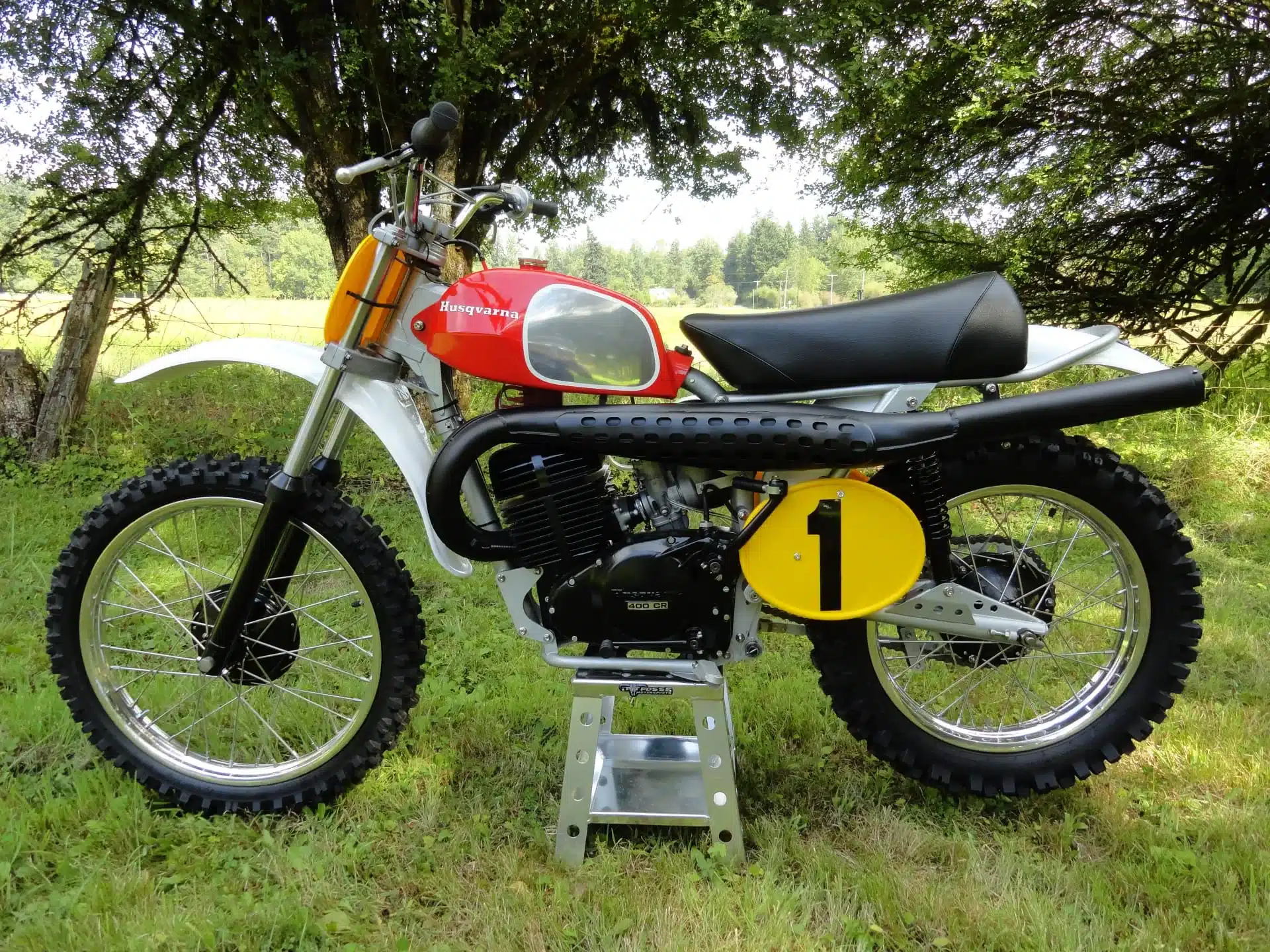 Seitenansicht einer 1972 Husqvarna Pro-Fab Works 400CR im Freien, klassische Motocross-Maschine mit rotem Tank und Startnummernplatte.