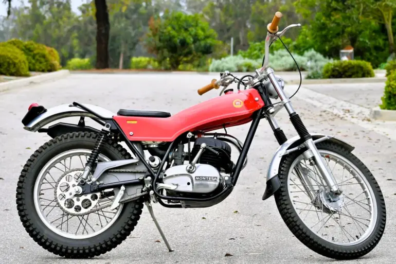 Seitenansicht einer roten 1972 Montesa Cota Enduro Trials mit Geländeprofil, abgestellt auf Asphalt.