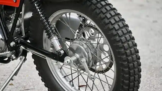 Nahaufnahme des Hinterrades einer Montesa Cota Enduro Trials von 1972 mit Stollenreifen und Kettentrieb.