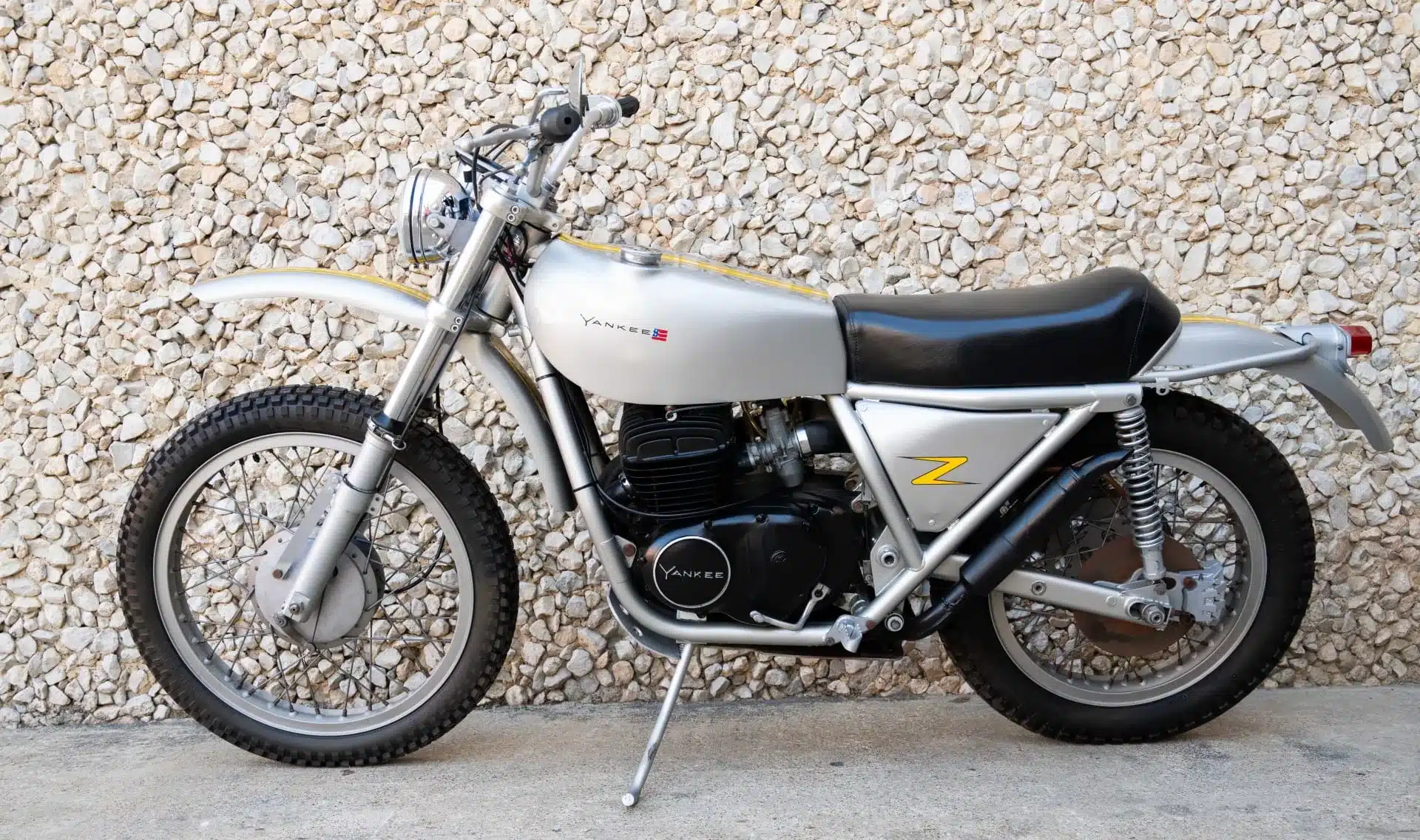 Seitenansicht einer silbernen 1972 Yankee Z500 Enduro vor einer Steinwand, Klassiker mit Paralleltwin-Motor.