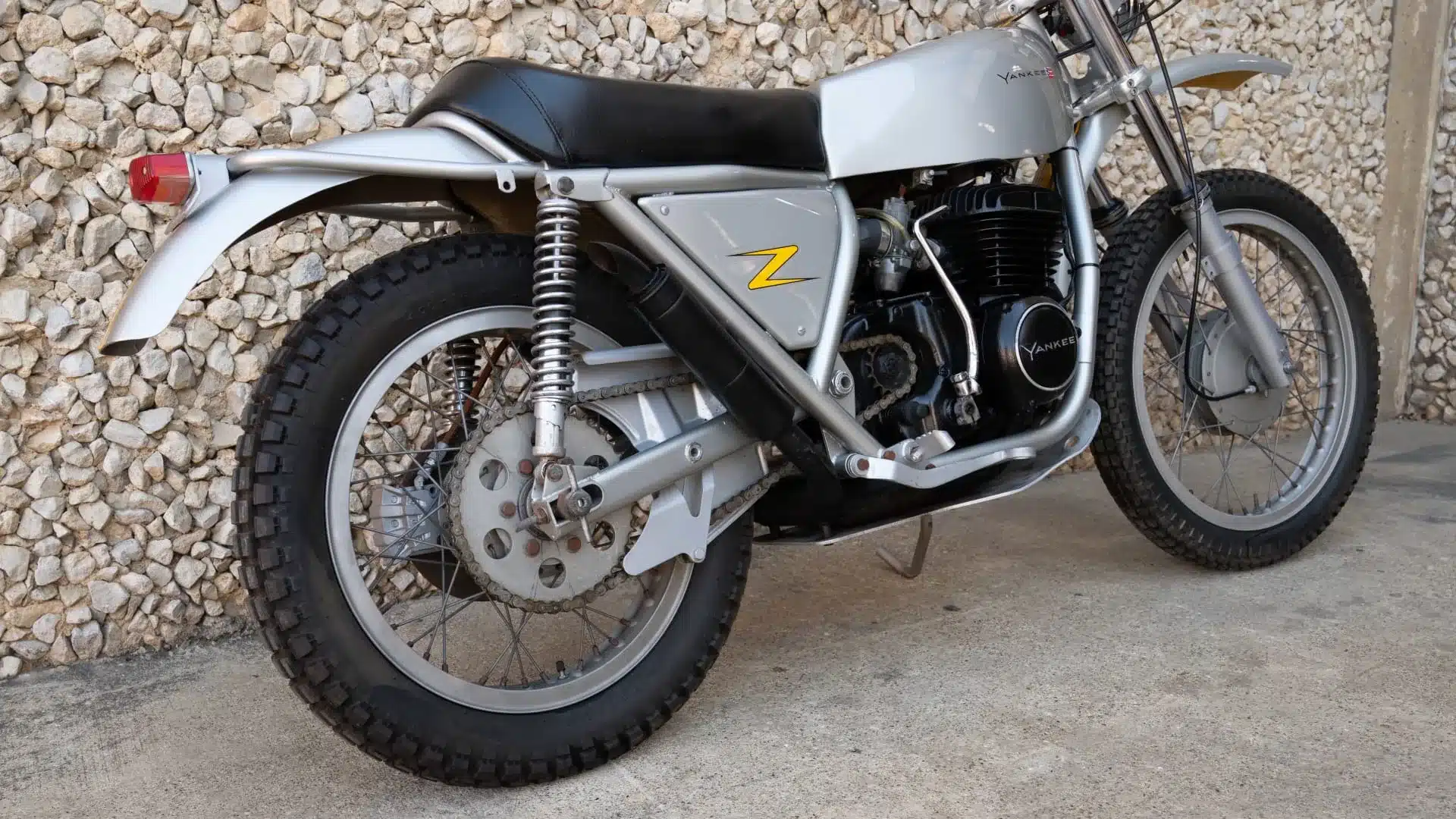 Seitenansicht einer silbernen 1972 Yankee Z500 Enduro mit schwarzem Sitz und gelbem Z-Logo vor Steinwand.