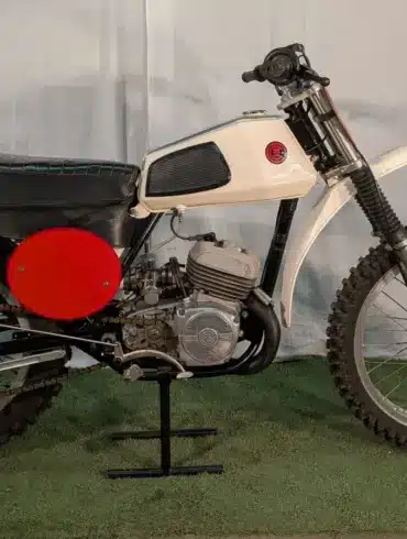 Seitenansicht einer 1973 CZ 125 Motocross mit weißem Tank, rotem Seitendeckel und Offroad-Bereifung.