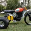 1973 Husqvarna Super Cycle 450 CR 3-Wheeler mit rotem Tank und gelber Startnummer im Gras stehend