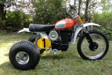 1973 Husqvarna Super Cycle 450 CR 3-Wheeler mit rotem Tank und gelber Startnummer im Gras stehend