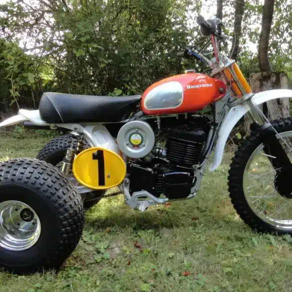 1973 Husqvarna Super Cycle 450 CR 3-Wheeler mit rotem Tank und gelber Startnummer im Gras stehend
