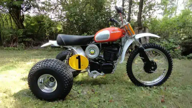 1973 Husqvarna Super Cycle 450 CR 3-Wheeler mit rotem Tank und gelber Startnummer im Gras stehend