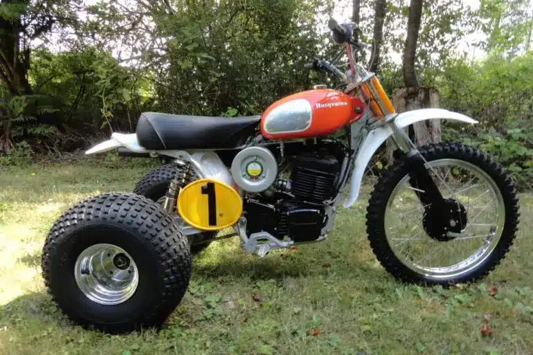 1973 Husqvarna Super Cycle 450 CR 3-Wheeler mit rotem Tank und gelber Startnummer im Gras stehend