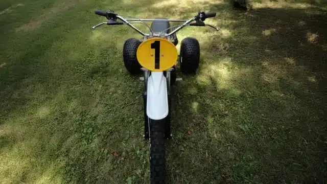 Vorderansicht eines 1973 Husqvarna Super Cycle 450 CR 3-Wheelers mit gelber Startnummer 1 auf Gras