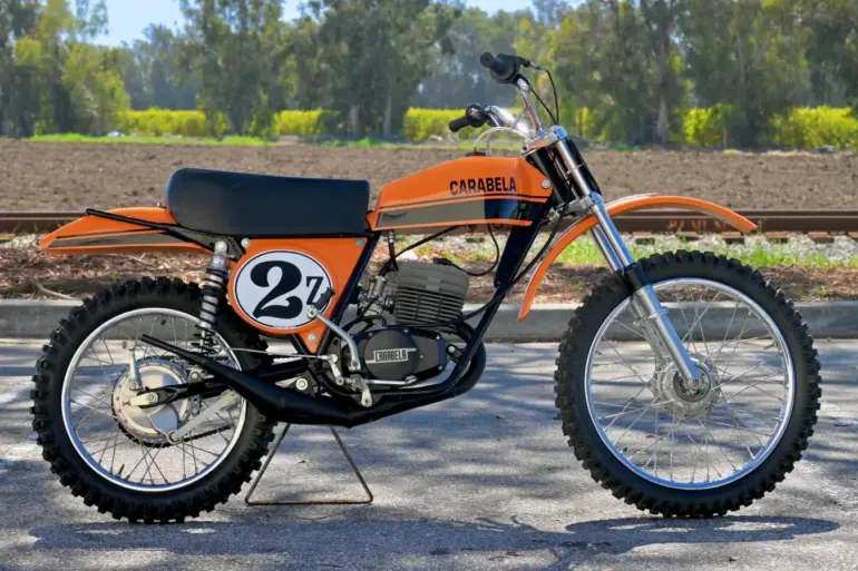 1974 Carabella 125 Motocross im Originalzustand, Seitenansicht mit orange-schwarzem Tank und Startnummer 27.