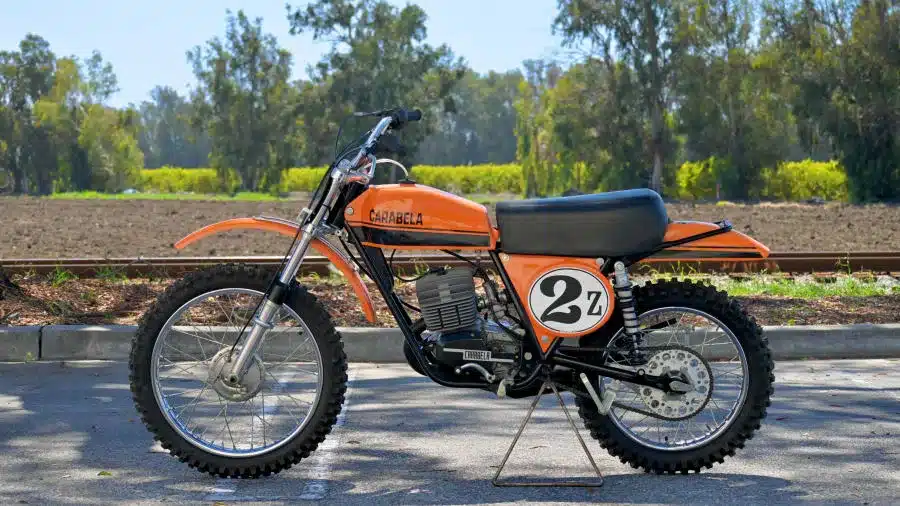 Seitenansicht einer 1974 Carabella 125 Motocross vor natürlicher Kulisse, vollständig restauriertes Offroad-Motorrad in Orange-Schwarz.