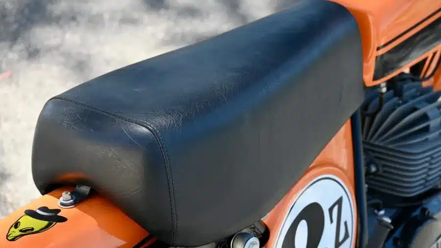 Schwarze Sitzbank auf einem orangefarbenen Rahmen der 1974 Carabella 125 Motocross mit sichtbarem Motor und Nummernschild