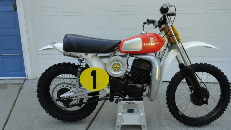 Seitenansicht einer 1974 Husqvarna 400 CR Motocross-Maschine mit rotem Tank und Startnummernschild.