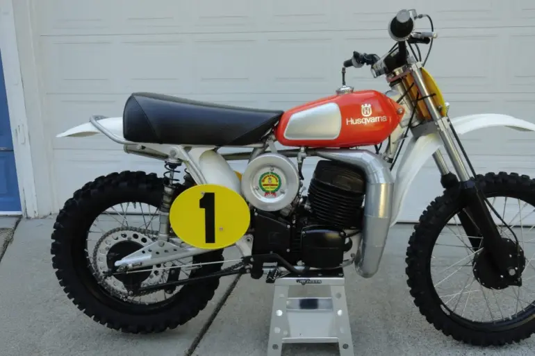 Seitenansicht einer 1974 Husqvarna 400 CR Motocross-Maschine mit rotem Tank und Startnummernschild.