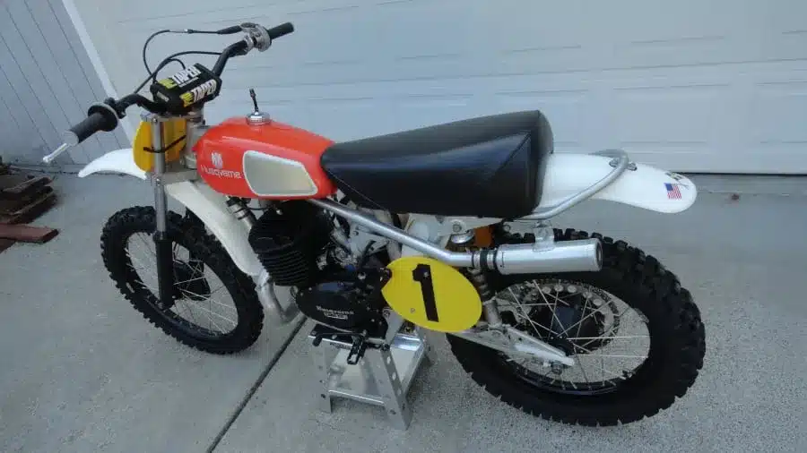 Motocross-Motorrad Husqvarna 400 CR Baujahr 1974 mit rotem Tank und Startnummer, Seitenansicht auf Betonboden.