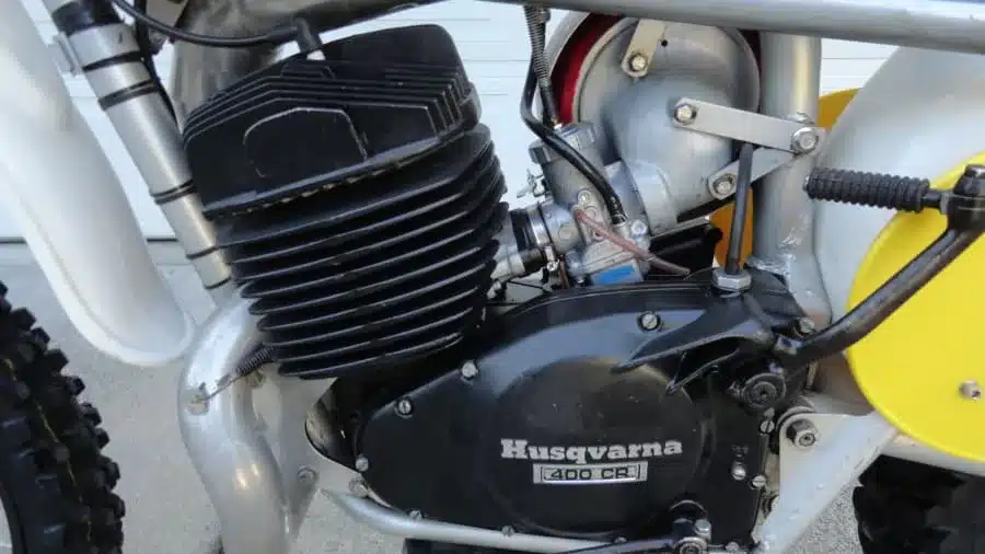 Nahaufnahme des Motors einer originalgetreuen 1974 Husqvarna 400 CR, Baugruppe mit schwarzem Motorgehäuse und sichtbarer Fahrwerksstruktur.