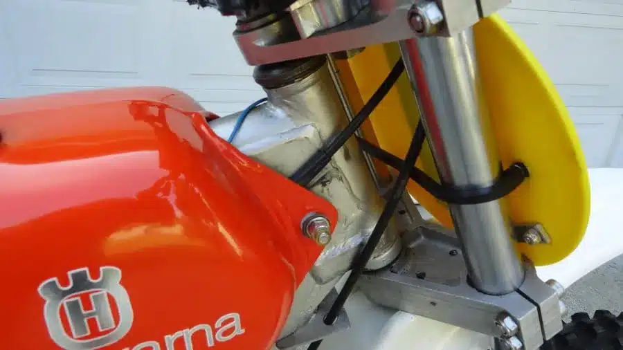 Detailansicht des Rahmens und Gabelbereichs einer klassischen Husqvarna 400 CR von 1974 mit rotem Tank und gelbem Schild